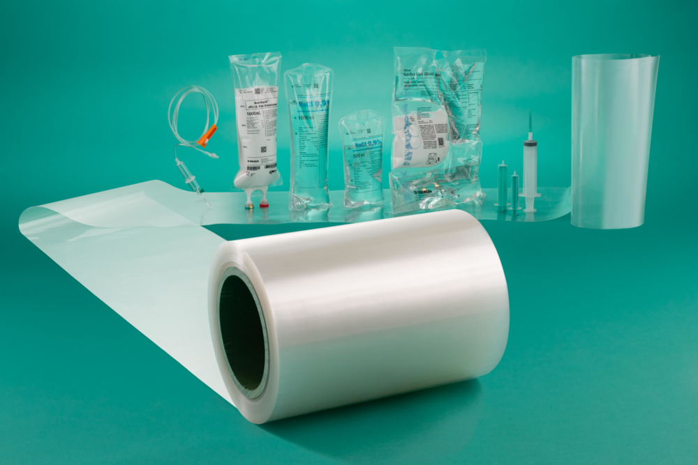 Les fournitures médicales telles que les sacs à perfusion, les seringues et les tubes sont présentées sur un fond bleu sarcelle avec un rouleau de film plastique transparent devant.