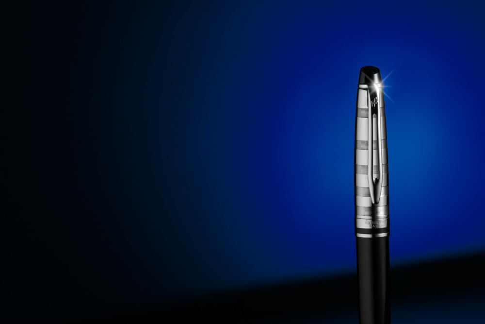 Un stylo plume fantaisie argenté et noir se tient debout sur un fond bleu avec une petite ombre.