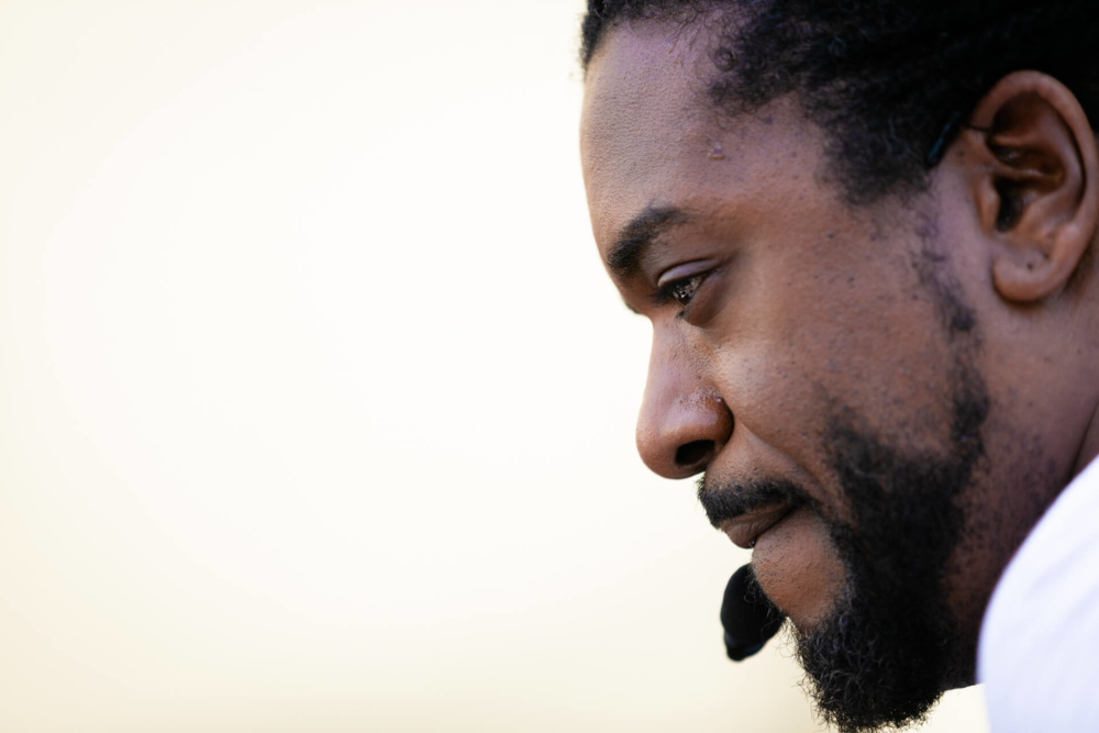 Gros plan du profil d'un homme afro-américain réfléchi sur un arrière-plan légèrement flou aux couleurs chaudes.