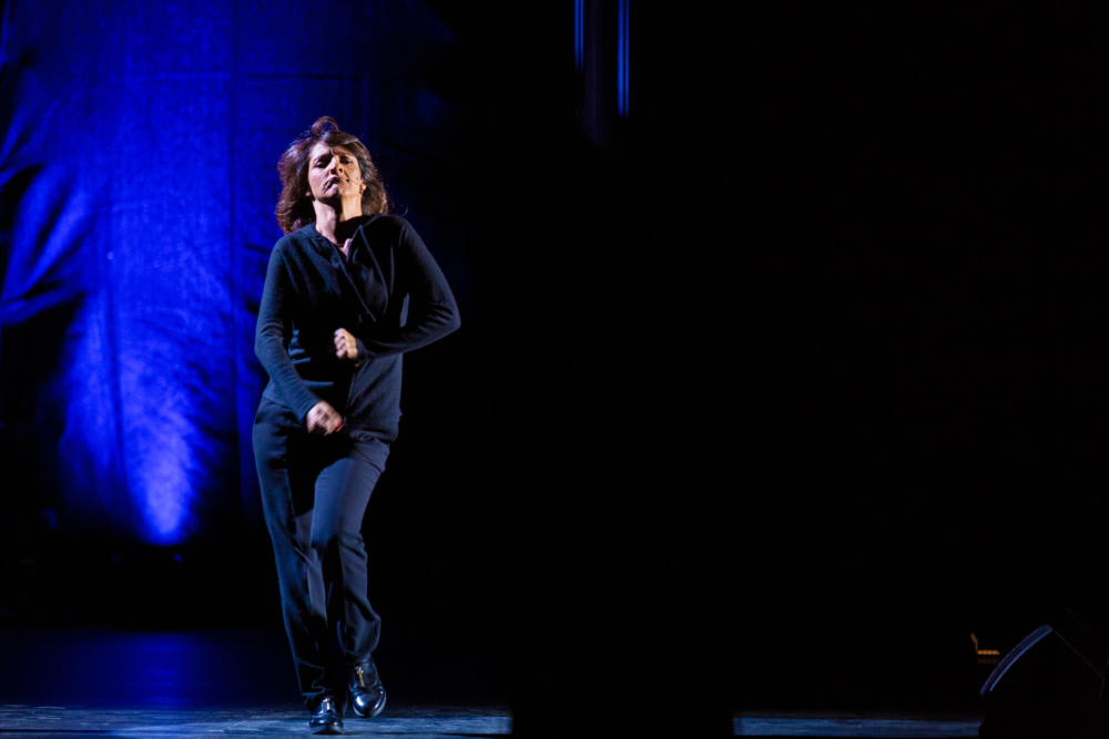 Un chanteur se produit avec passion sur une scène mal éclairée, chantant intensément dans un micro sous un seul projecteur.