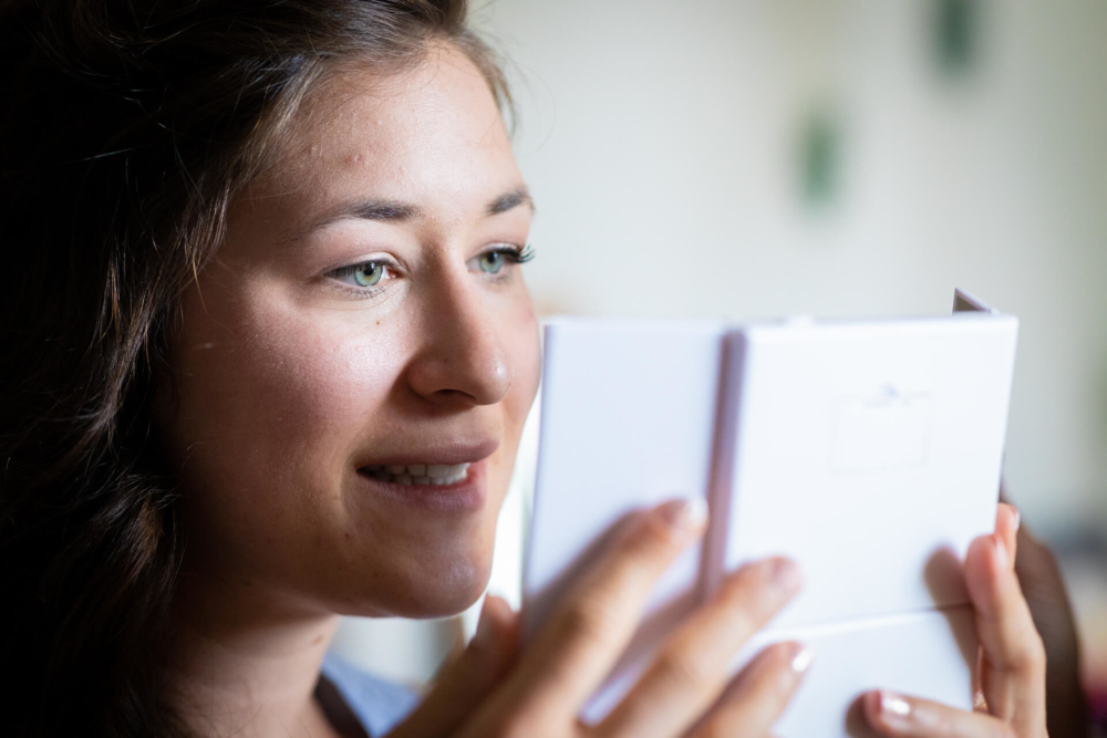 Une jeune femme souriante lit un petit livre blanc. Elle est étroitement concentrée sur ce qu'il y a à l'intérieur. Une lumière douce illumine ses traits.