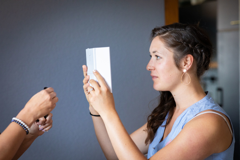 Une femme, les cheveux attachés, portant des boucles d'oreilles et un haut bleu, regarde attentivement un document blanc que tient quelqu'un d'autre dans un environnement professionnel.