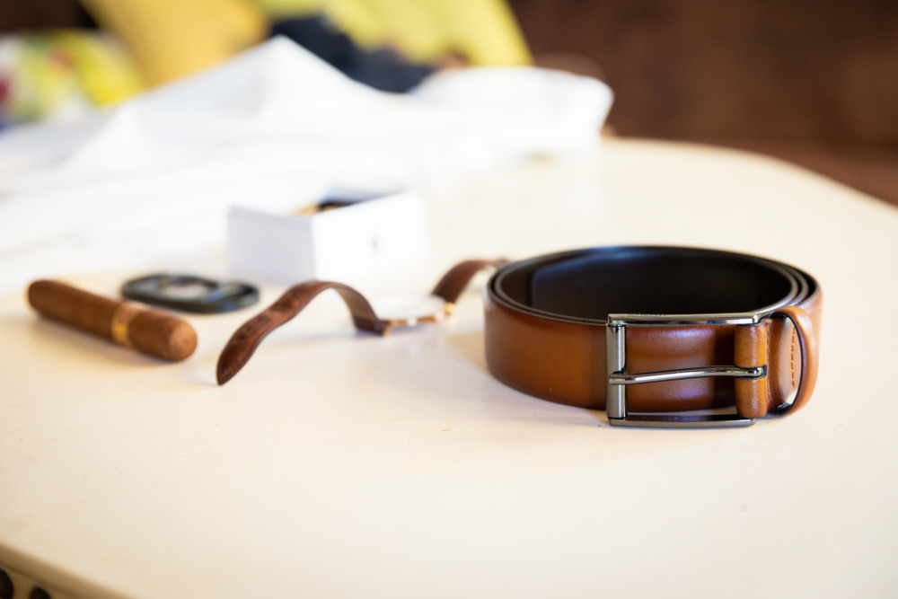 Une ceinture en cuir marron à boucle brillante est posée sur une table à côté d'une montre et de lunettes de soleil, constituant un ensemble élégant d'articles de mode.