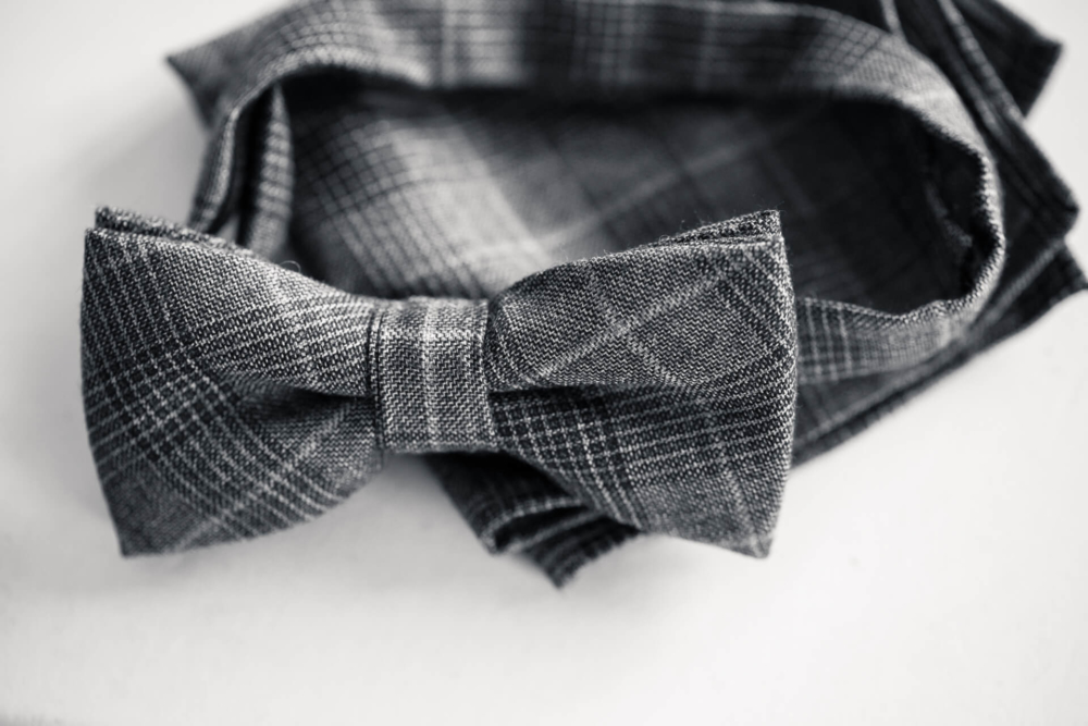 Une photo en noir et blanc montre une vue rapprochée d’un nœud papillon à carreaux gris. La cravate est confectionnée avec soin et est posée sur un tissu assorti.