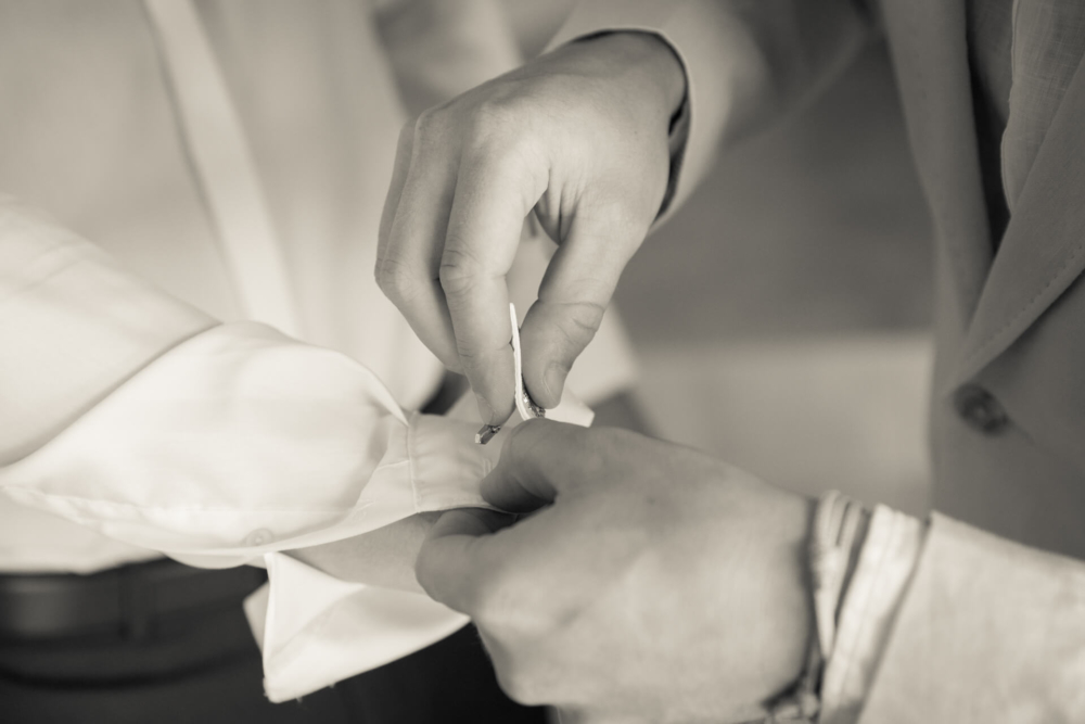 Photo en gros plan, en noir et blanc, d'une personne attachant un bouton de manchette sur la manche de sa chemise.