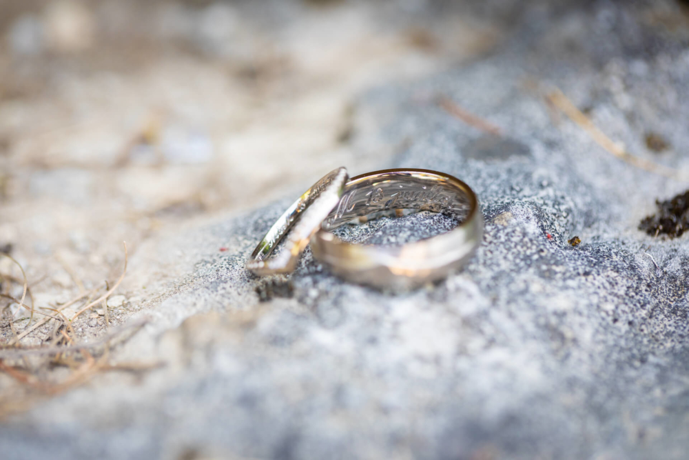 Deux alliances sont posées sur un rocher, l’une dans l’autre. Ils sont en partie recouverts de minuscules grains de sable et l'arrière-plan est flou. Cette scène est romantique et intime.
