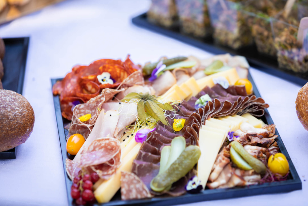 Un plateau de viande et de fromage raffiné avec cornichons et garnitures, soigneusement dressé sur un plateau de service noir.