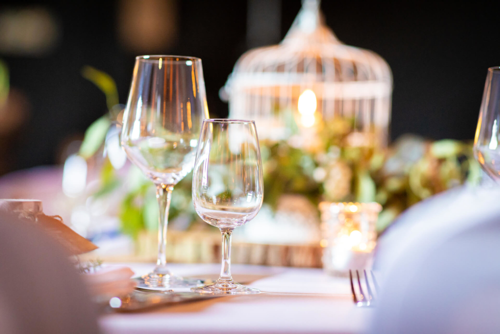 Un dîner raffiné avec des verres à vin en cristal transparent sur une table. Les lumières douces et les décorations floues en arrière-plan rendent le lieu chaleureux et accueillant.