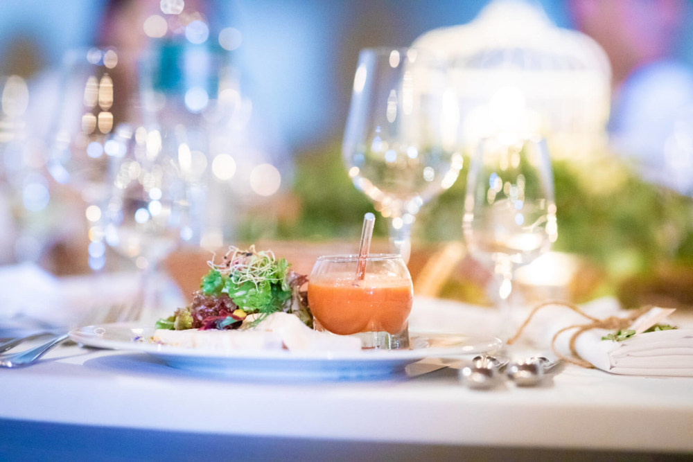 Un petit apéritif est élégamment présenté sur une table à manger, accompagné d'un cocktail muni d'une paille. La verrerie et le décor sur fond flou ajoutent de la sophistication.