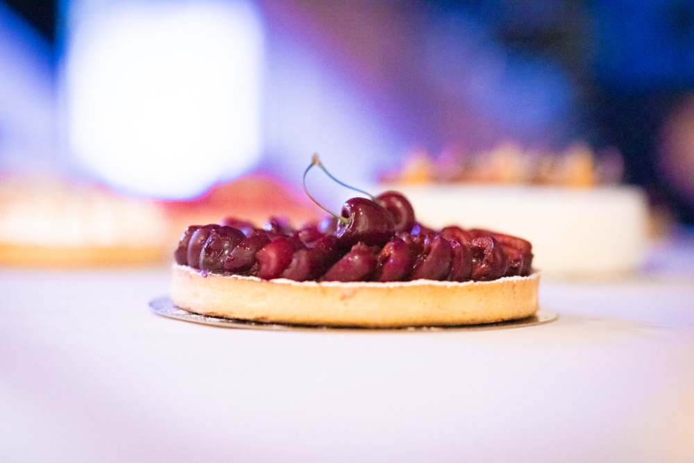 Une vue détaillée d'une tarte aux cerises sur une table, avec l'arrière-plan flou en raison des effets de lumière lors d'une réunion.