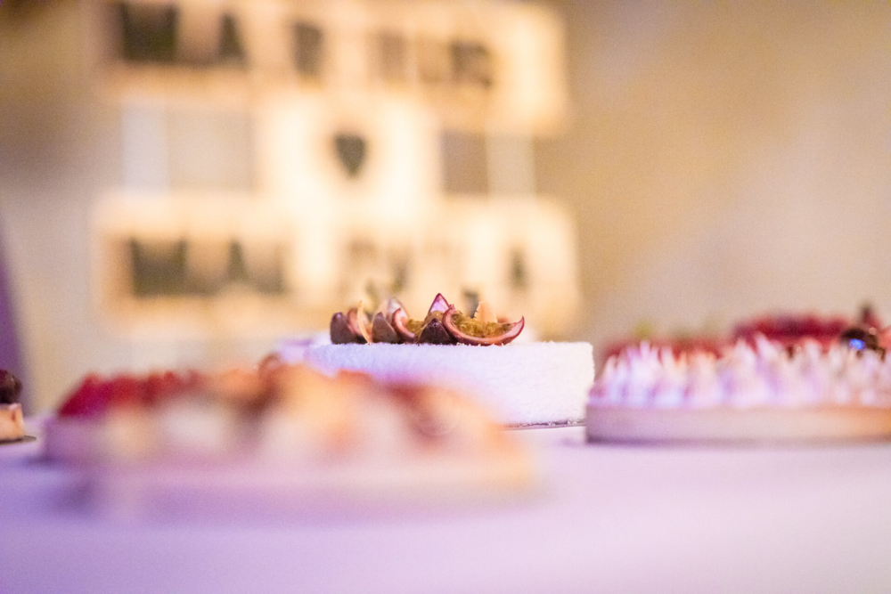 Une vue détaillée d'entrées garnies de figues sur des plateaux de service blancs fantaisie, présentées lors d'un dîner avec un éclairage doux et flou en arrière-plan.