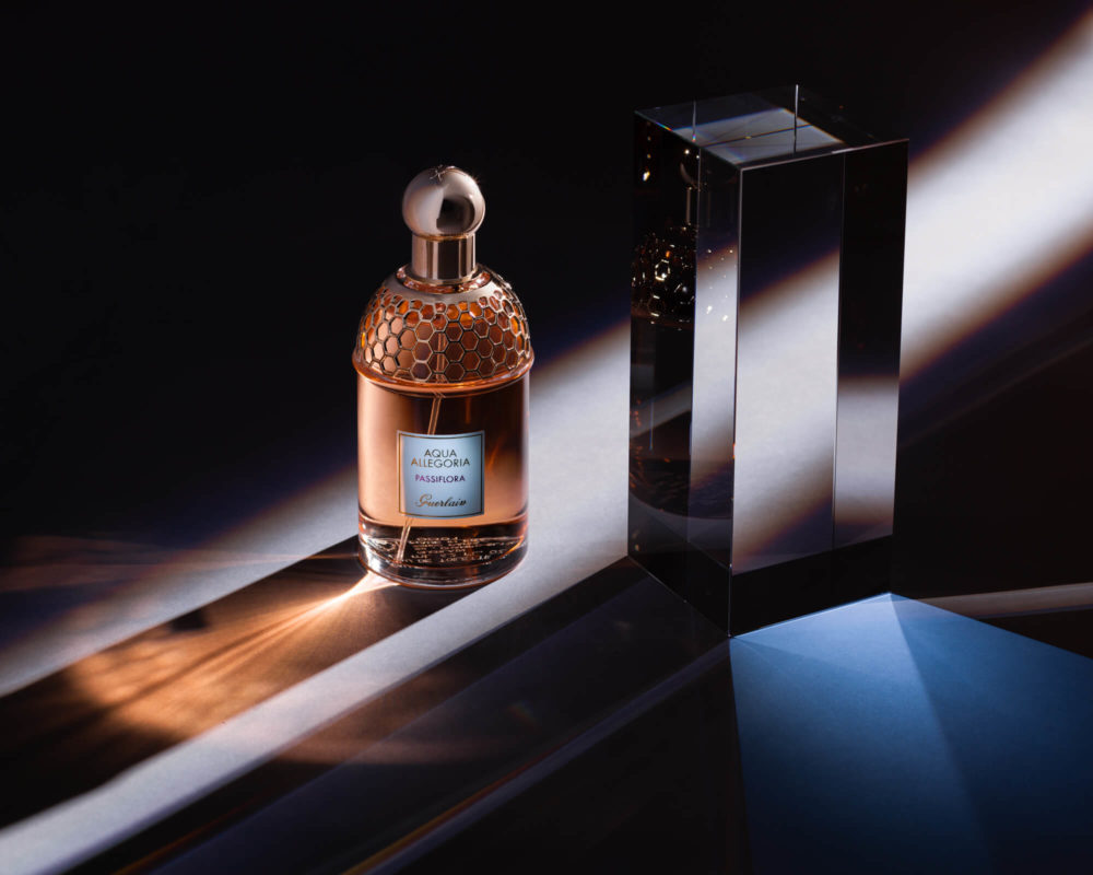 Un flacon de parfum fantaisie avec un motif en nid d'abeille et un récipient en verre brillant est sur un fond sombre avec des touches d'éclairage bleues et blanches.