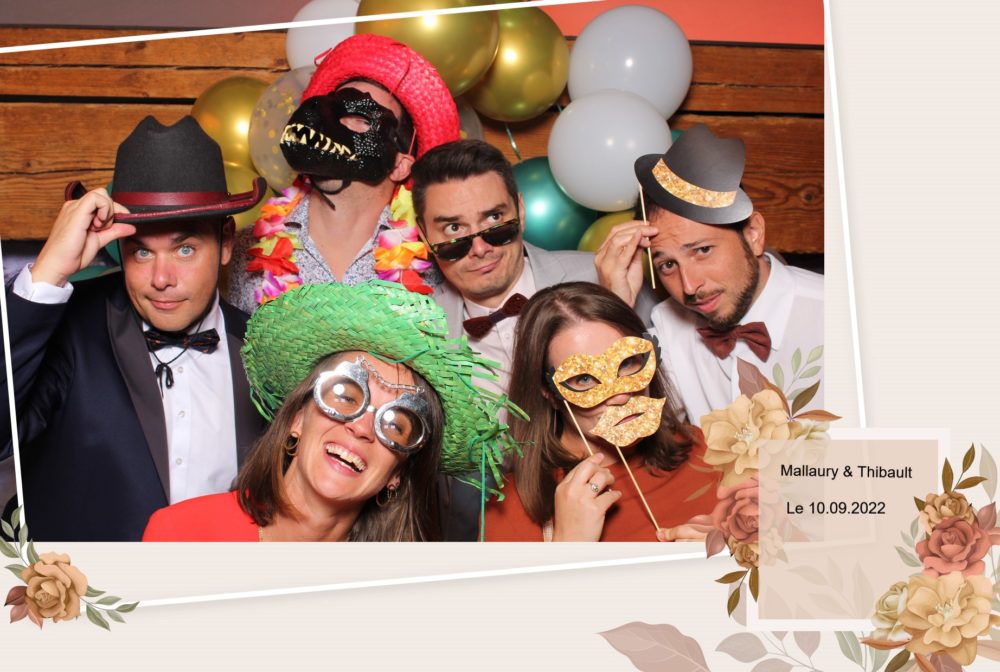 location de photobooth location de photomaton location de borne à selfie Slika Photography 4 Un groupe de six personnes s'amusent dans un photomaton de mariage en portant des accessoires amusants tels que des masques et des chapeaux. La photo montre une date d'événement et des noms indiquant une célébration.
