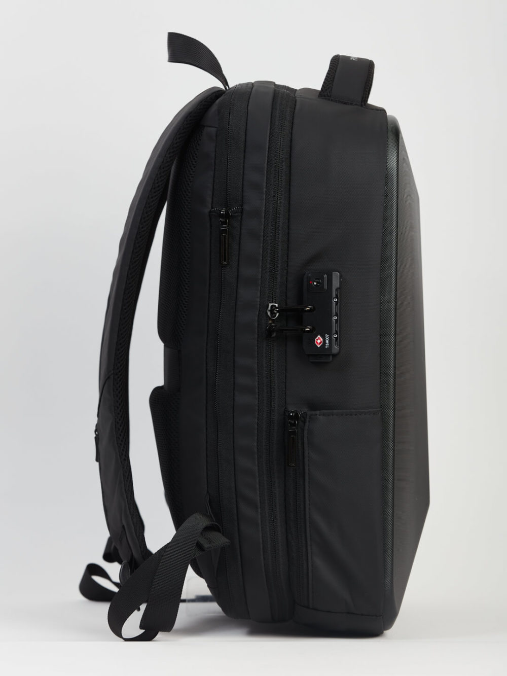 Vue latérale d'un sac à dos noir avec de nombreux compartiments et une serrure à combinaison, sur un simple fond blanc.