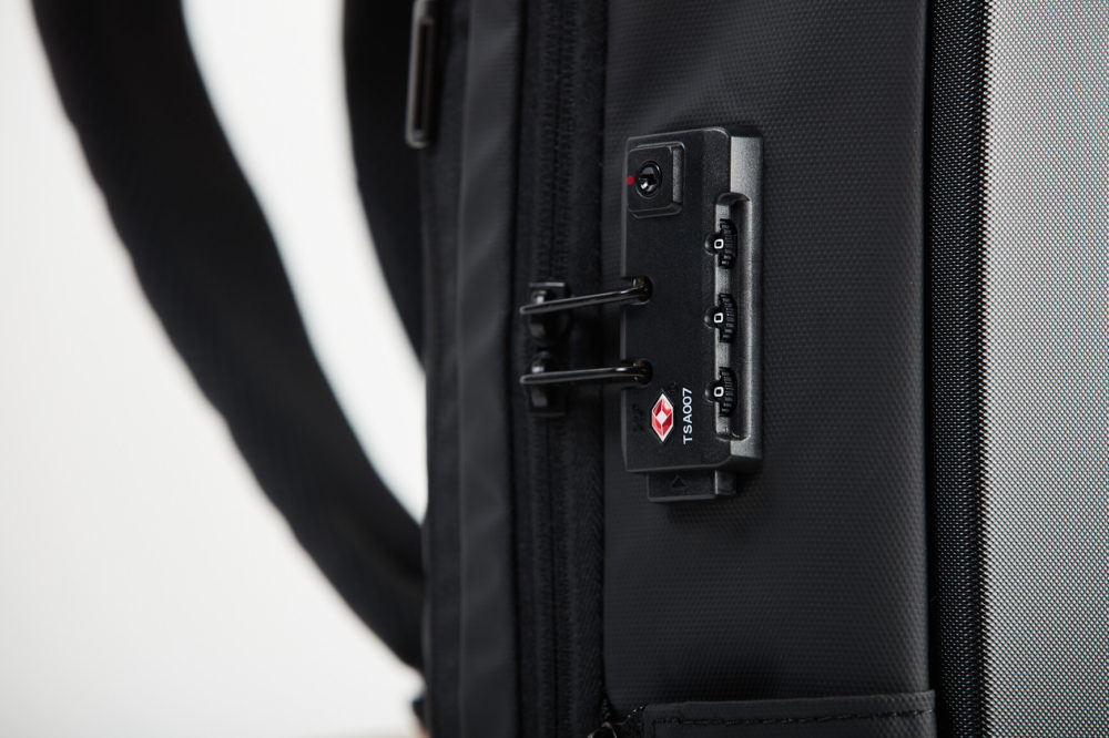 Vue rapprochée d'un cadenas de valise approuvé par la TSA avec un logo en losange rouge placé sur une valise noire, sur un fond gris clair.