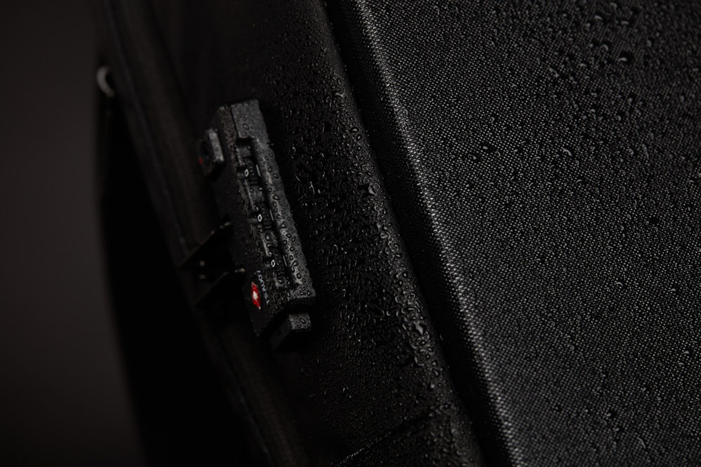 Image en gros plan d’une valise noire avec une serrure à combinaison. La surface texturée comporte de petites gouttelettes d'eau, ce qui indique qu'elle a récemment été sous la pluie.