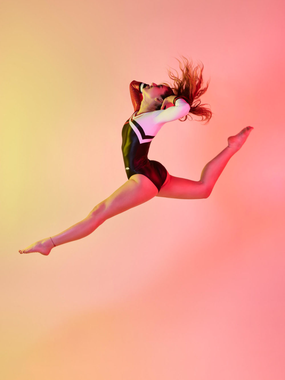 photographe sport yoga bien-être fitness danse slika photography 006 Une danseuse, prise au milieu d'un saut vigoureux sur un fond rose et jaune. Lorsqu'elle fait un saut de ballet, ses cheveux s'étalent.