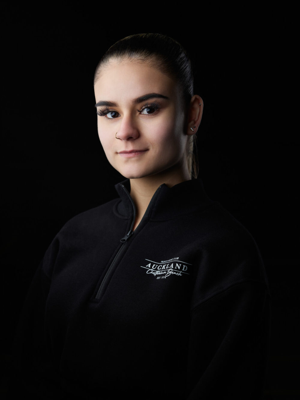 photographe sport yoga bien-être fitness danse slika photography 020 Une femme avec une coiffure tressée, vêtue d’une veste de gymnastique Auckland noire, pose avec assurance sur un fond sombre.