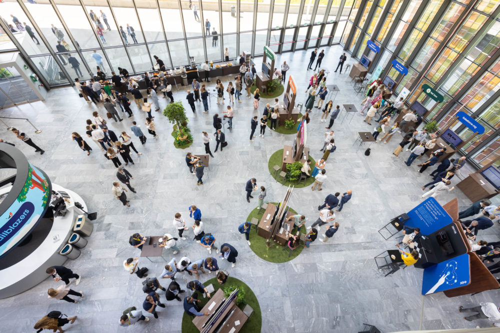 Plan aérien d'un événement d'entreprise animé dans un bâtiment contemporain où les participants interagissent autour de stands d'exposition et de sièges.