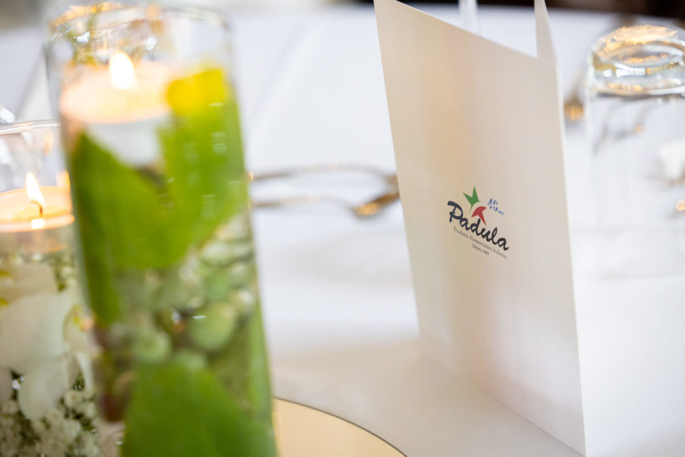 Il s'agit d'une vue détaillée d'une élégante table à manger, montrant une carte de menu sur laquelle est écrit « padella », accompagné d'un logo vibrant. L'arrangement comprend des verres, des bougies et de délicates décorations florales.