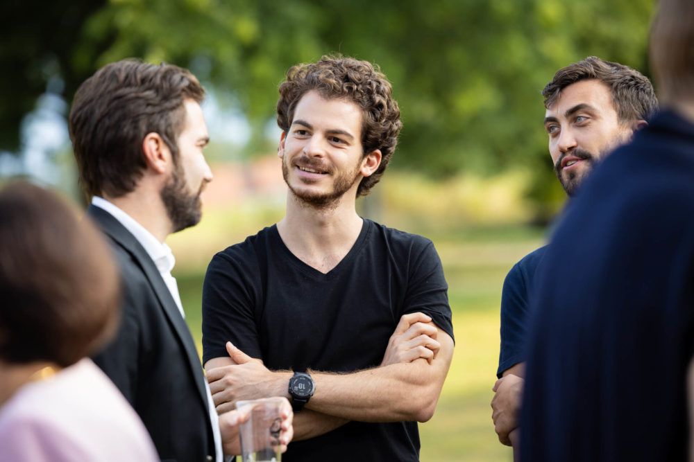 Un groupe de jeunes adultes discutent à l’extérieur et une personne sourit en écoutant un orateur.