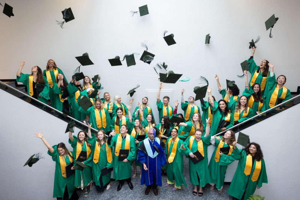 Un groupe joyeux d'étudiants diplômés en robes vertes et jaunes jettent leurs casquettes en l'air dans les escaliers, célébrant leur réussite.