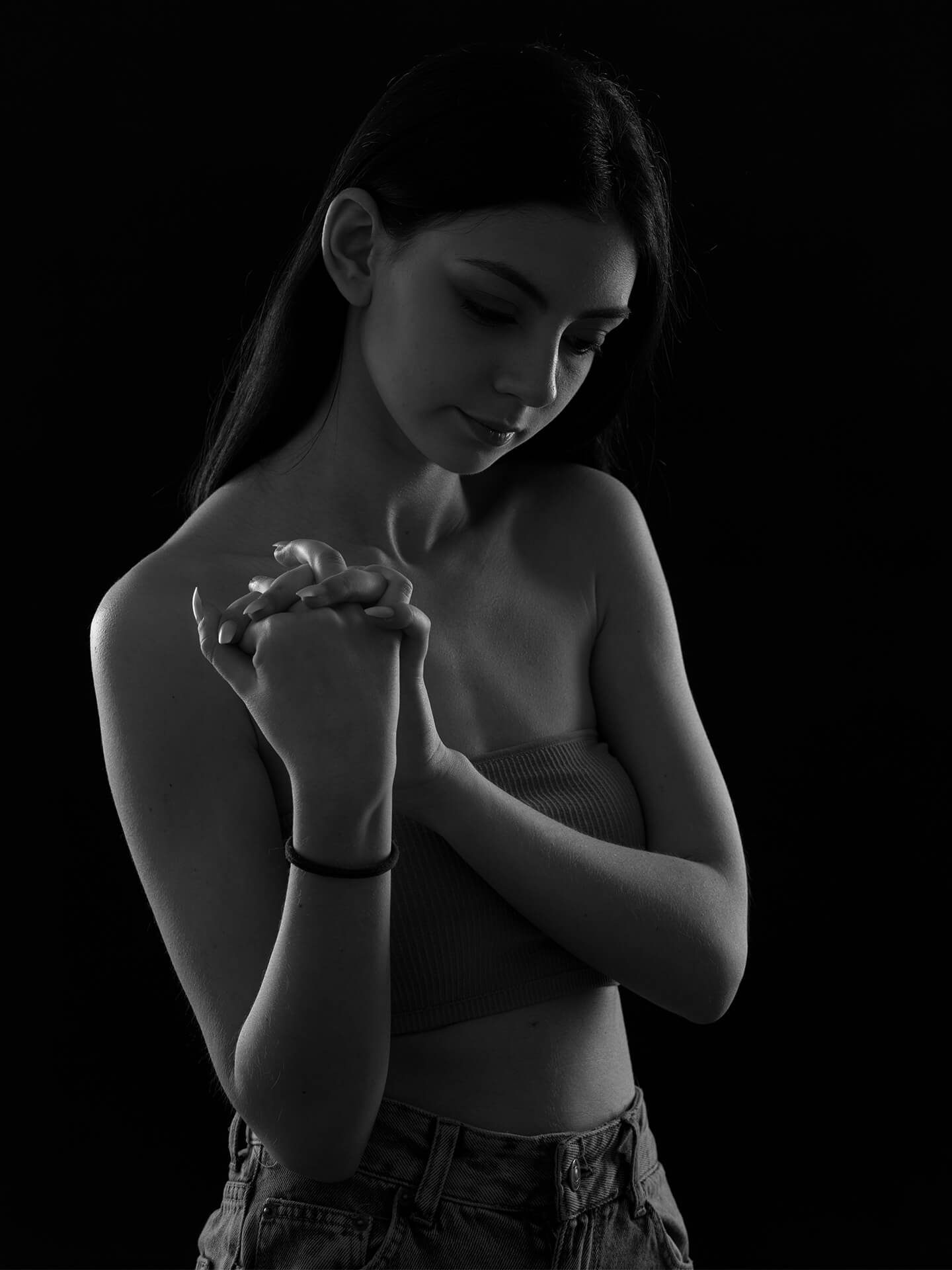 Une description simple serait la suivante : une jeune femme pose pensivement sur une photo en noir et blanc. Elle a les mains jointes et les yeux fermés, sur un fond sombre.