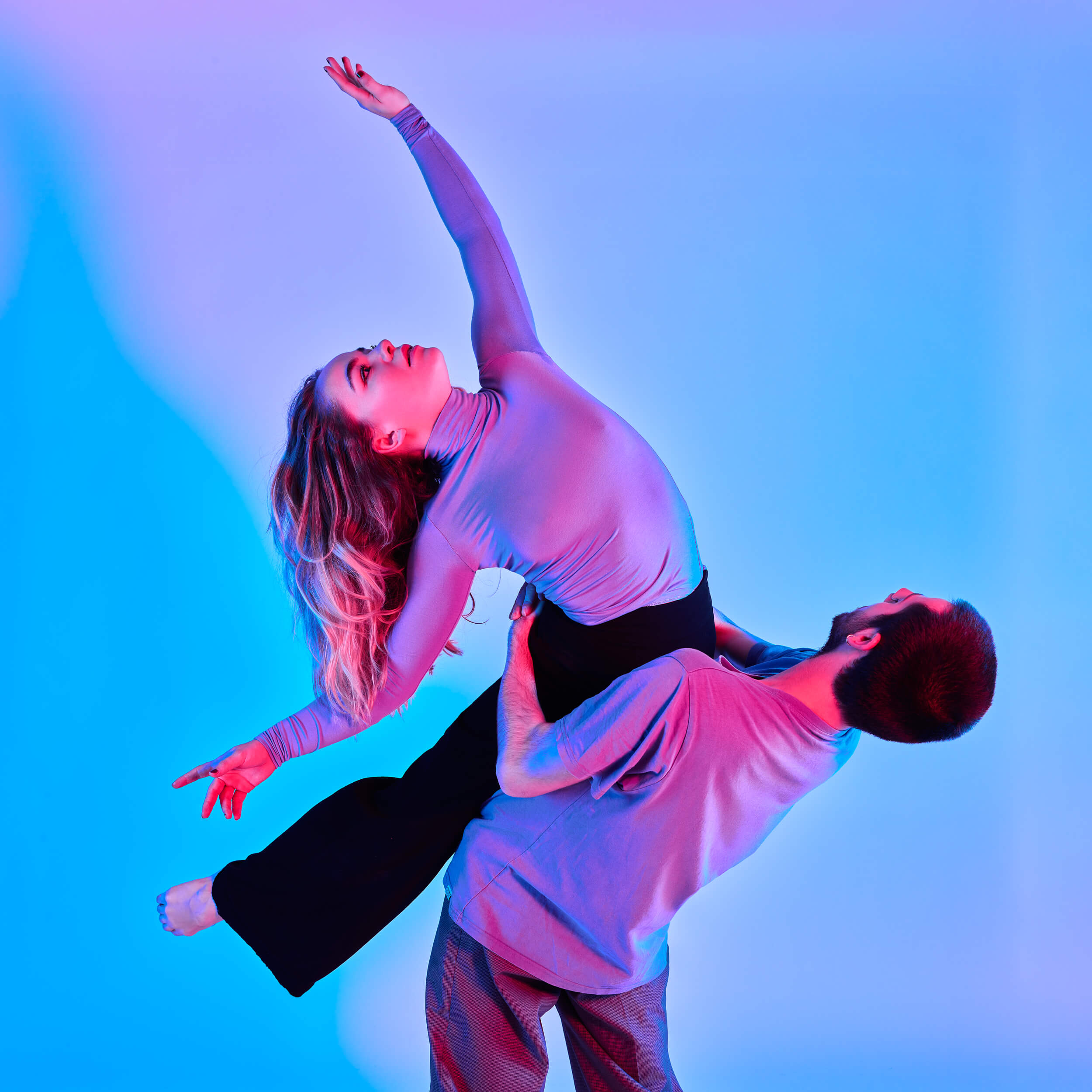 Slika Photography Lausanne Photographe Professionnel Figure Danse 3 Un homme et une femme dansent avec entrain sous des lumières bleues et roses. La femme est magnifiquement penchée sur le dos de l'homme.